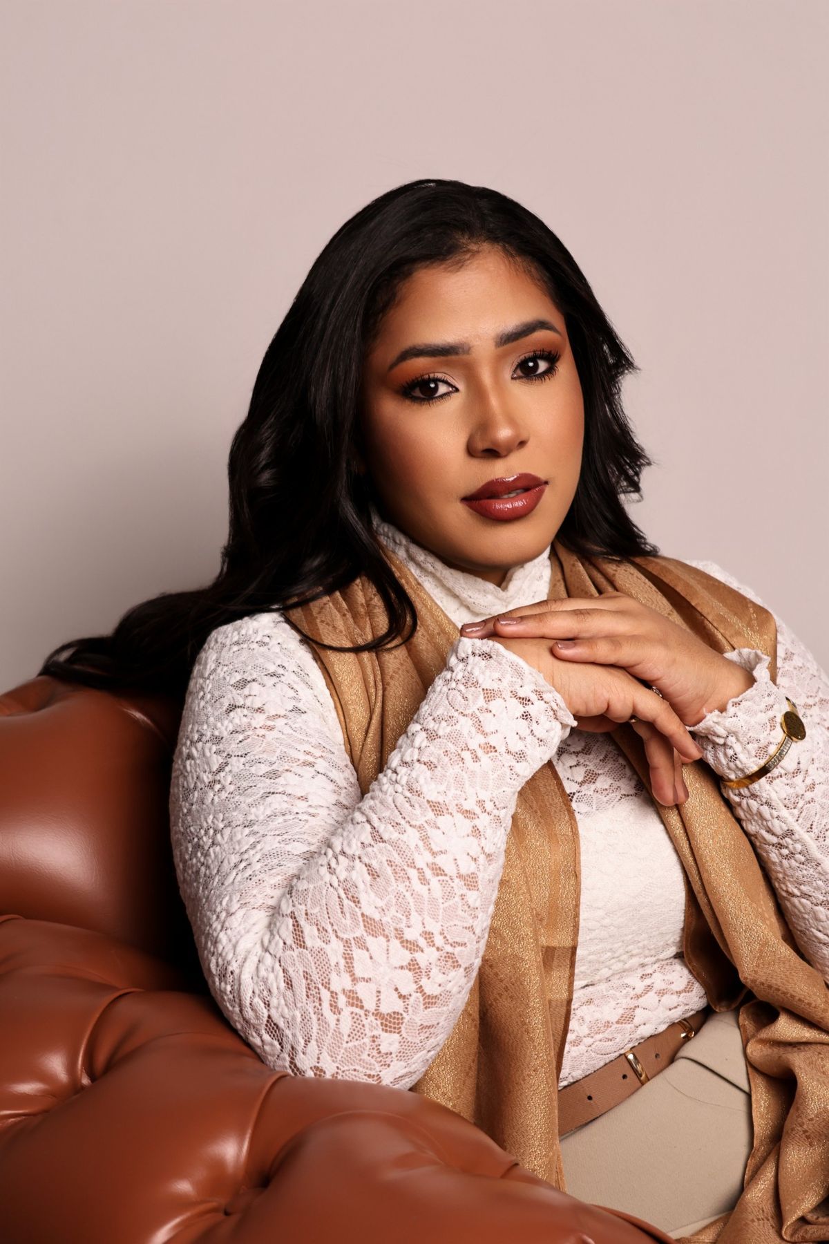 Retrato de mulher de renda branca e xale dourado sentada em sofá de couro