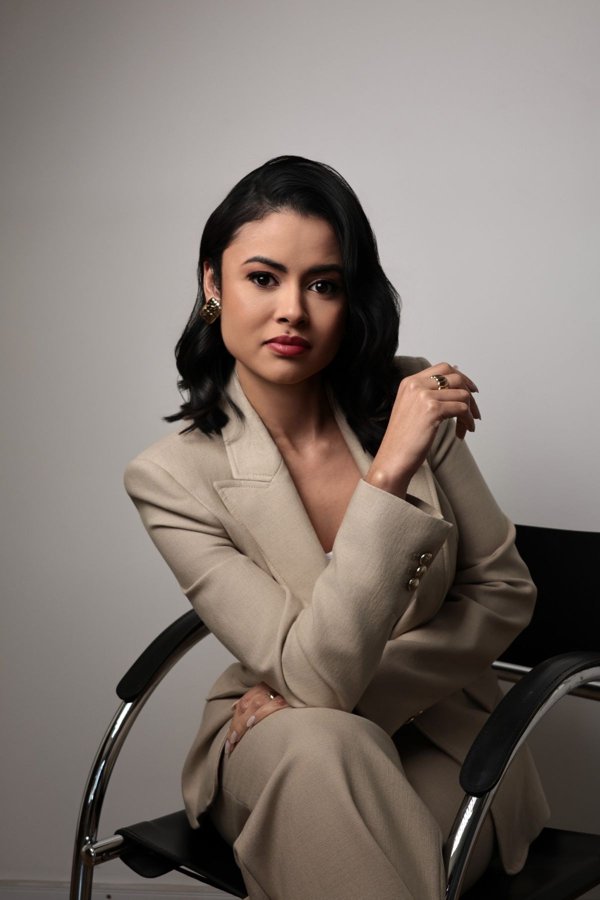 Retrato de mulher de terno bege sentada em cadeira de design
