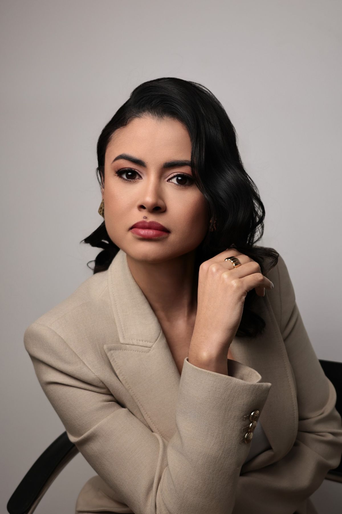 Retrato de mulher de blazer bege com a mão junto ao cabelo