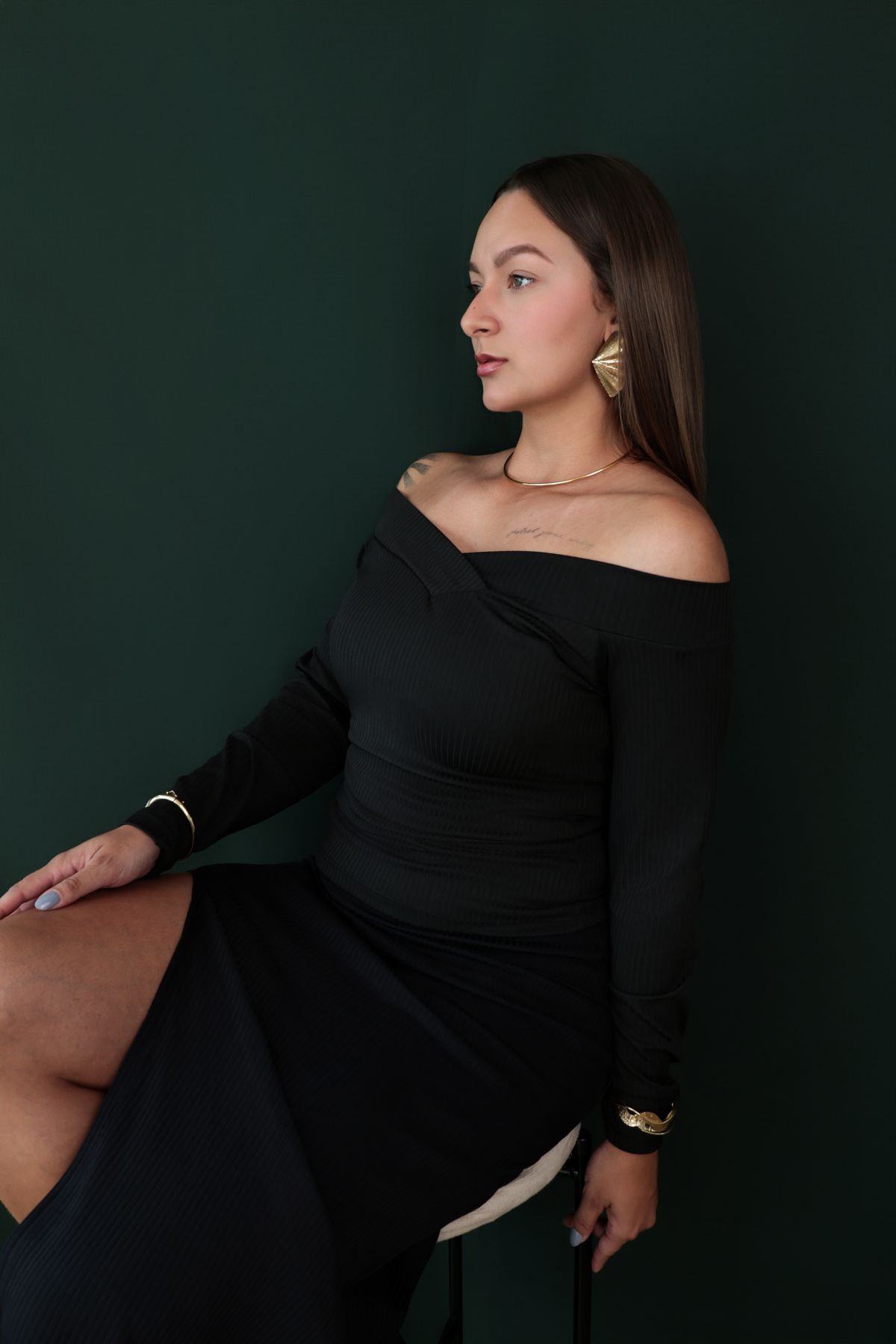 Modelo sentada de perfil em fundo verde profundo