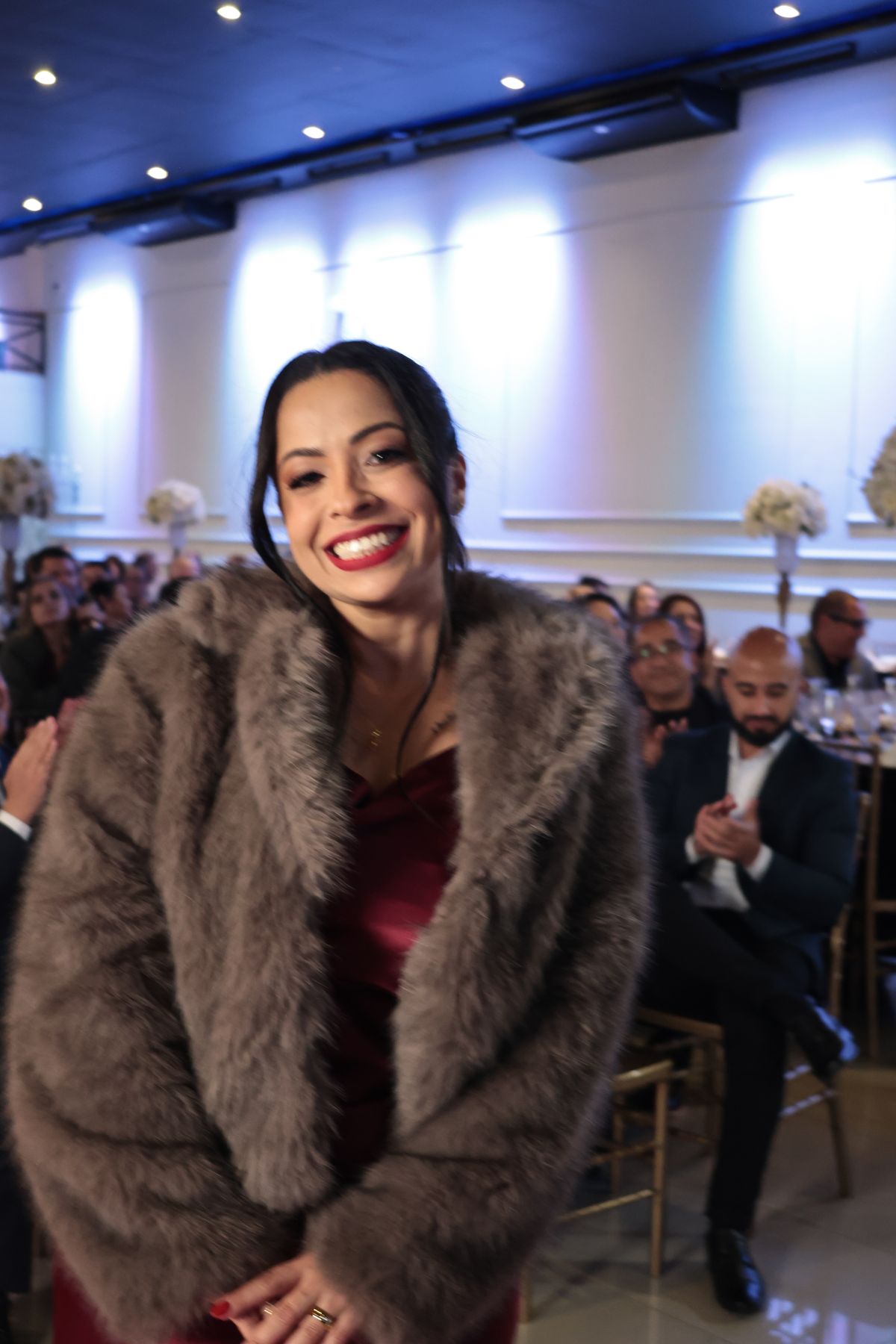 Convidada sorrindo de casaco de pele em jantar de gala